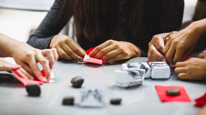 Students sit outside at a table learning origami, the ancient art of paper folding, in the 34th Street district in New York City.