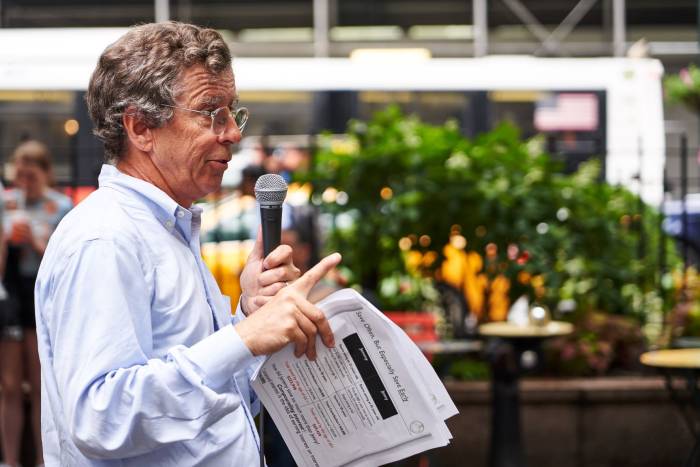 A finance professional stands in front of an outdoor class in Herald Square, New York City, teaching a free class on personal finance.