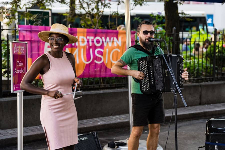 A woman and a man from Trio Arrebol play music outdoors in Greeley Square Park.