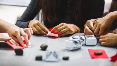 Students sit outside at a table learning origami, the ancient art of paper folding, in the 34th Street district in New York City.