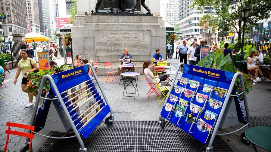 People sit at tables talking with a reading room cart nearby in Herald Square Park in New York City.